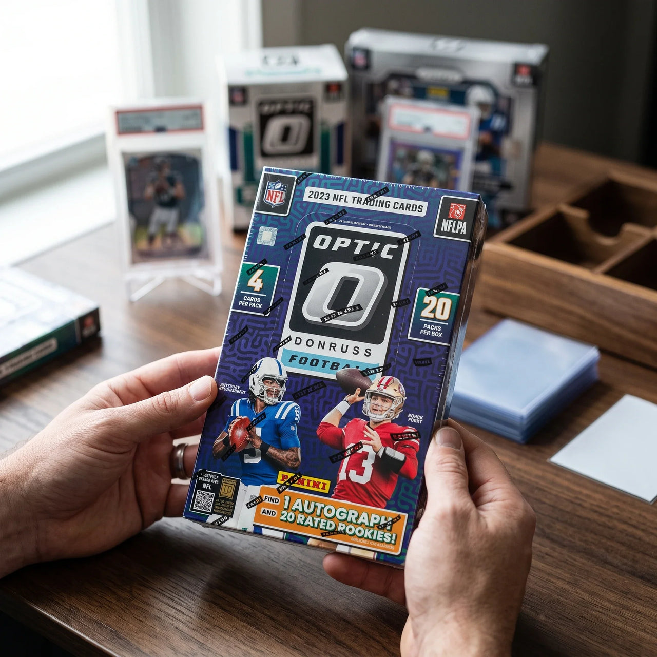 Collector hands displaying 2023 Panini Donruss Optic Football Hobby Trading Cards on a premium card-shop desk.