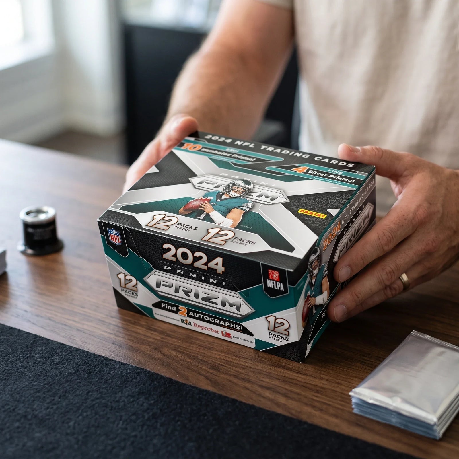Collector hands displaying 2024 Prizm Football RTYH /99 or Less - Rip Til You Hit on a premium card-shop desk.