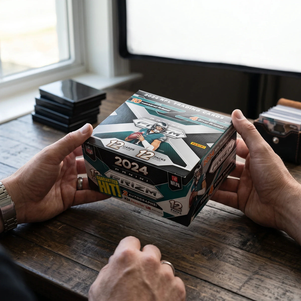 Collector hands displaying 2024 Prizm Football RTYH /99 or Less - Rip Til You Hit on a premium card-shop desk.
