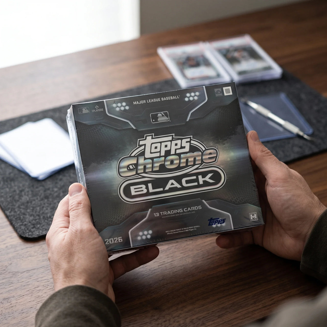 Collector hands displaying 2026 Topps Chrome Black Baseball Hobby Trading Cards LV on a premium card-shop desk.