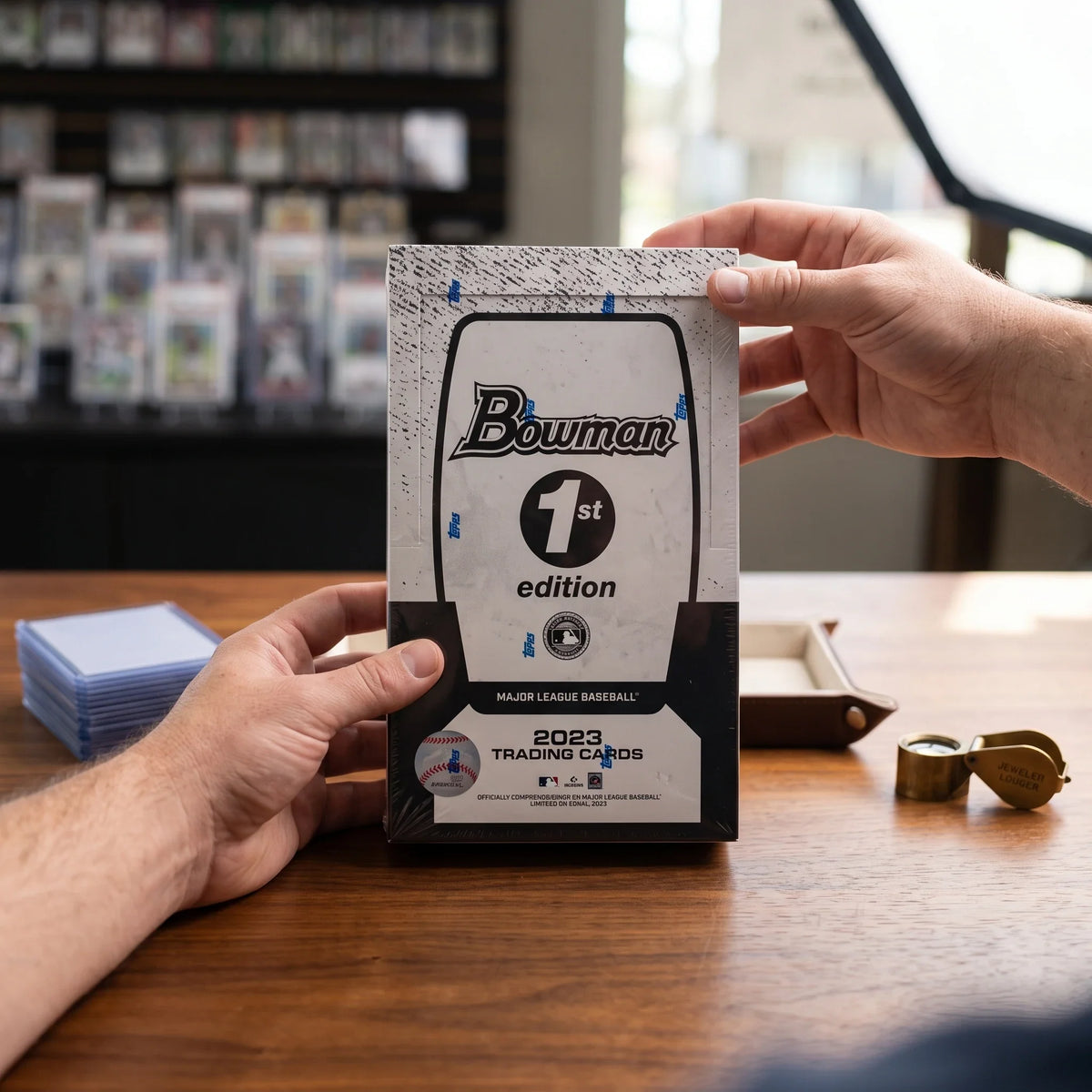 Collector hands displaying 2023 Bowman Baseball 1st Edition 12 Box Lot Prospect Cards (Ships Sealed Only) on a premium card-shop desk.
