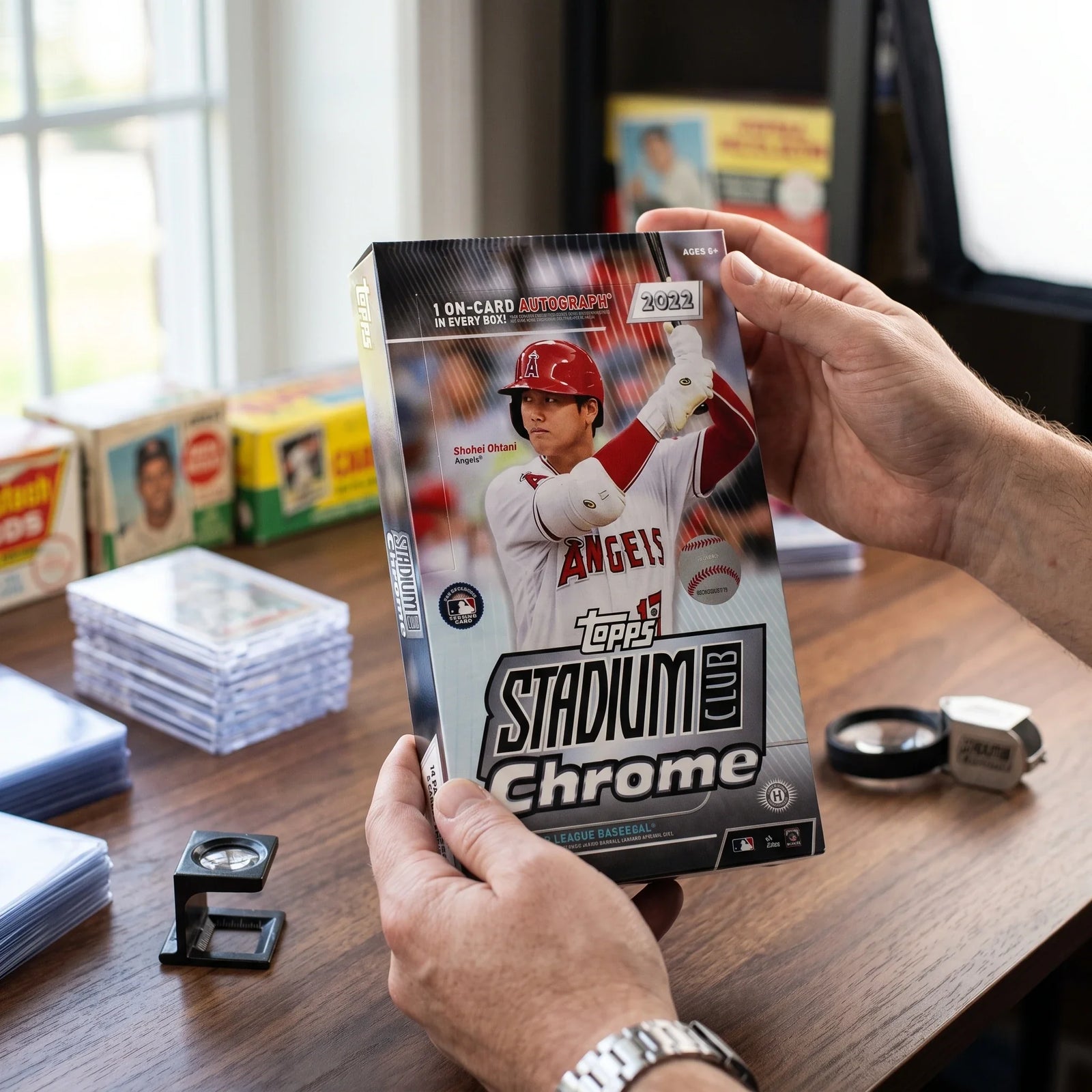 Collector hands displaying 2022 Topps Stadium Club Chrome Baseball Hobby Box (Ships Sealed Only) on a premium card-shop desk.