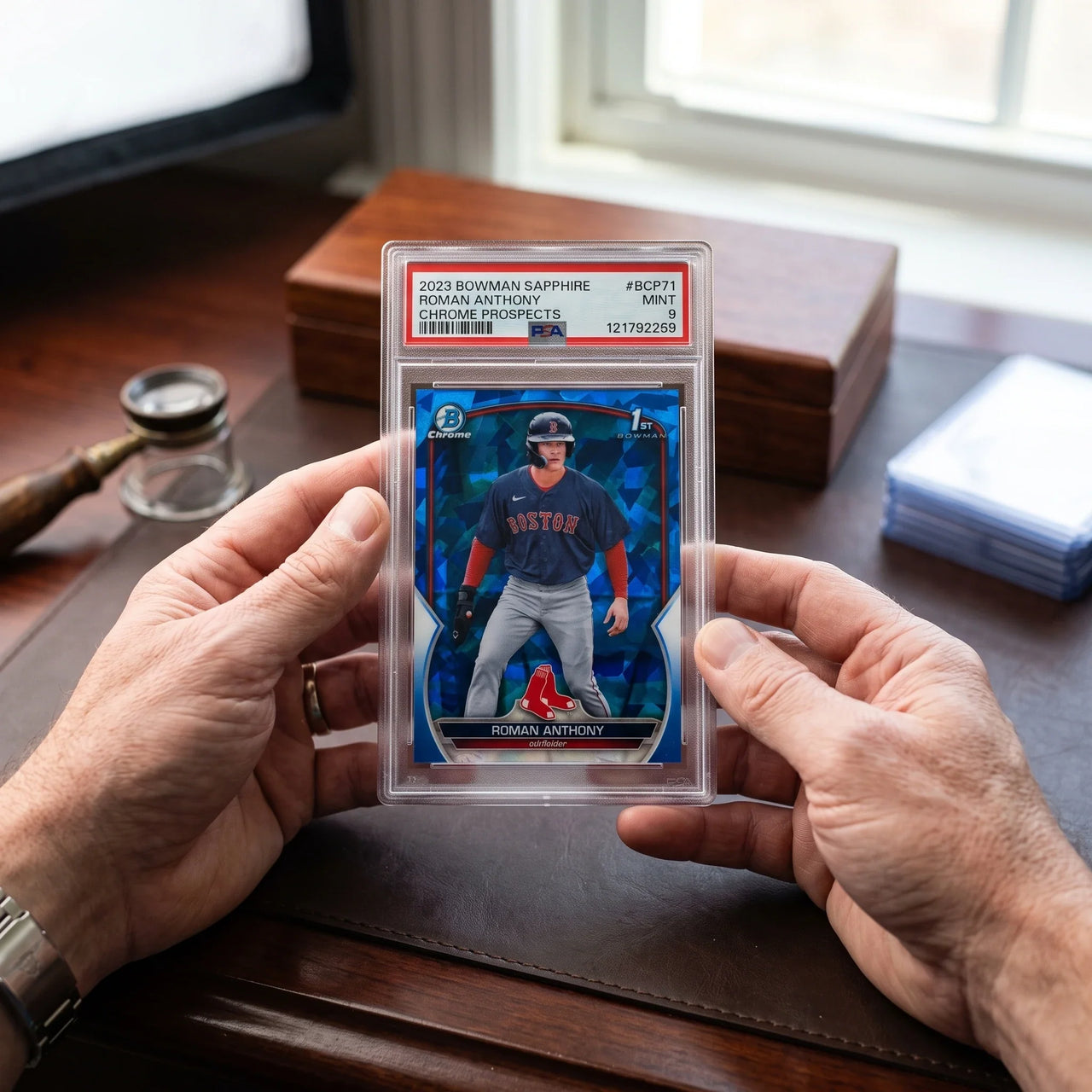 Collector hands displaying Roman Anthony 2023 Bowman Chrome Sapphire Rookie Card | PSA 9 on a premium card-shop desk.
